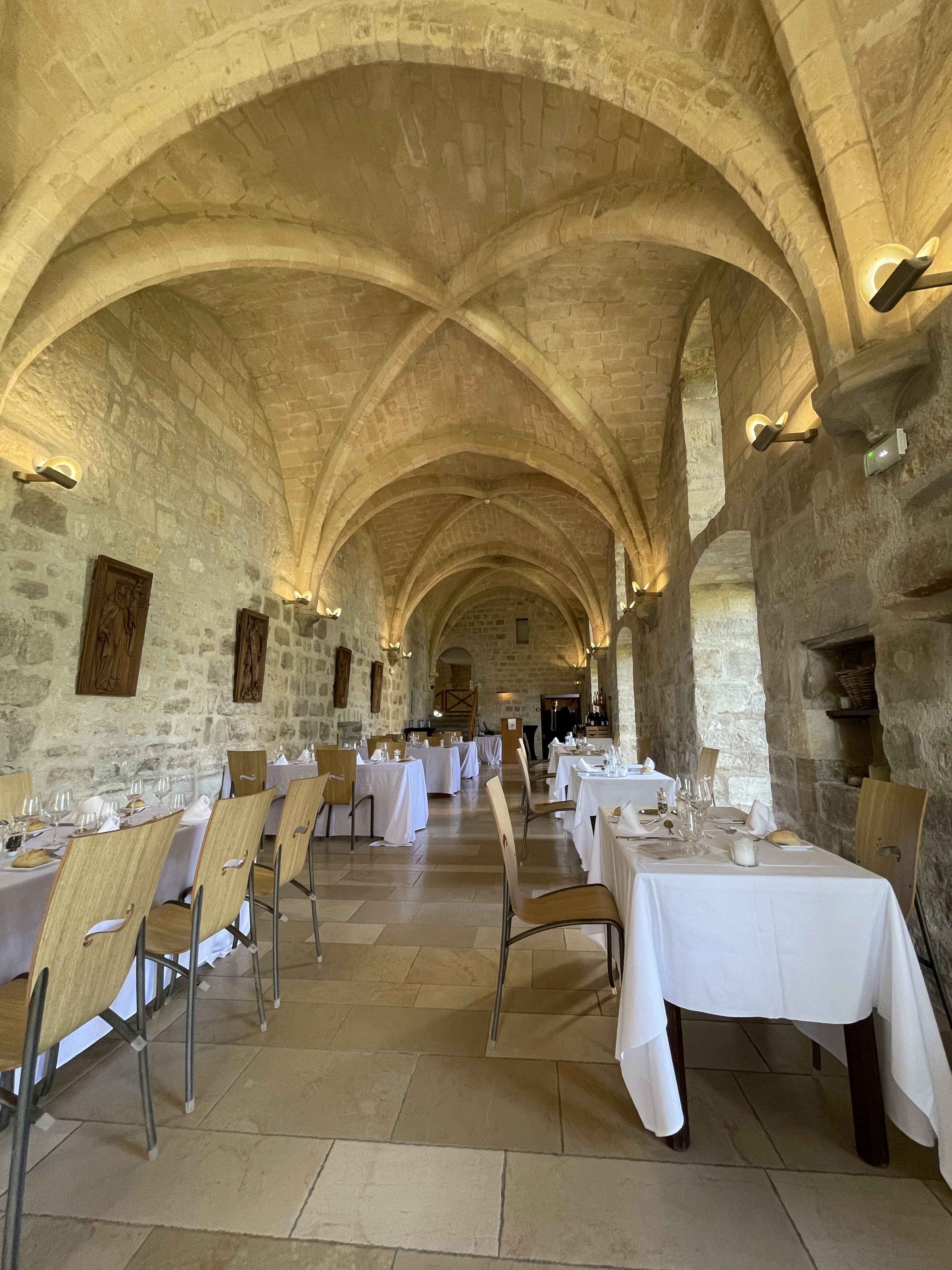 Intérieur d'un restaurant avec des tables décorées de nappes blanches et des chaises en bois, sous une voûte en pierre.