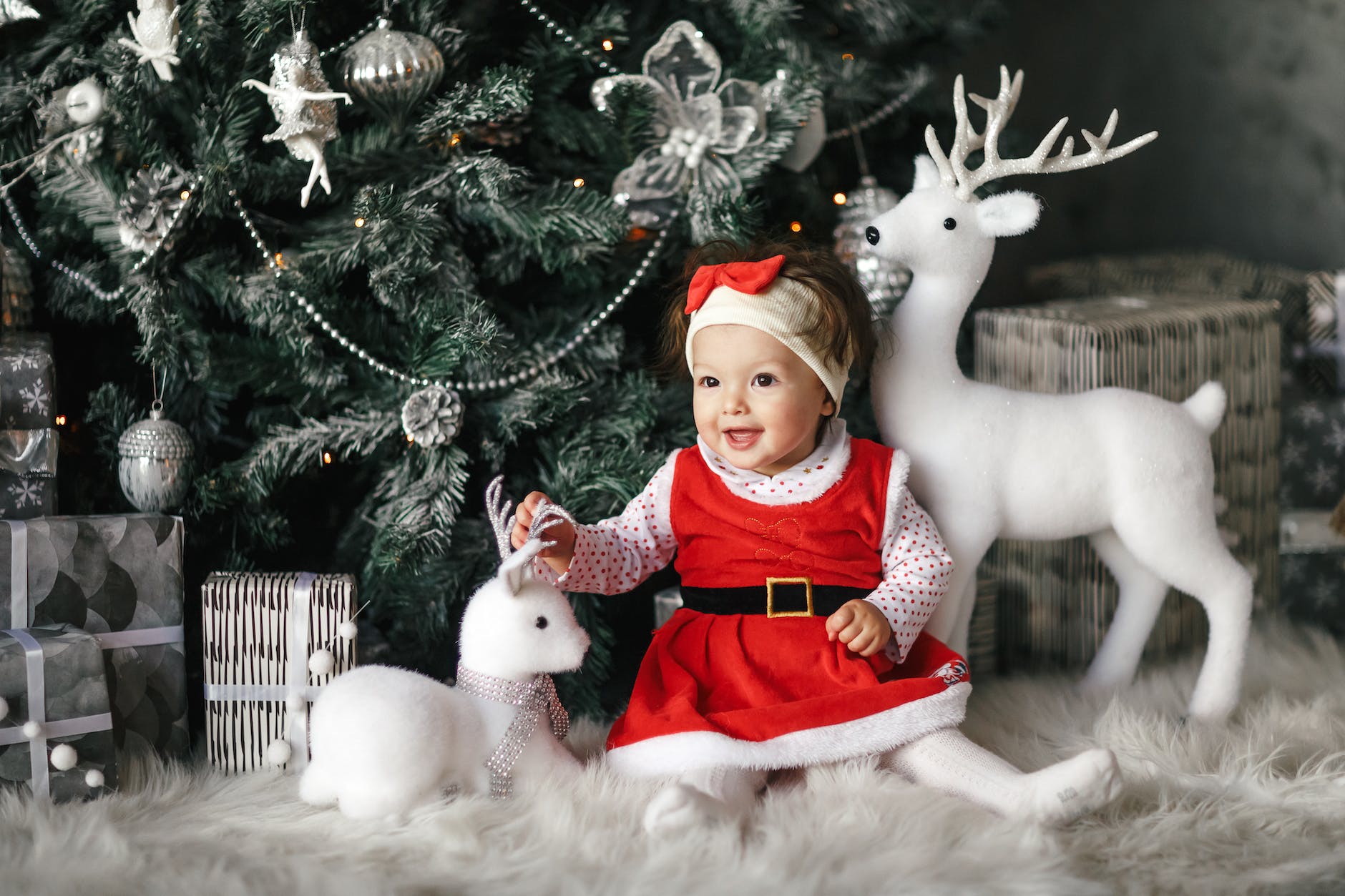 baby girl wearing santa dress sitting beside christmas tree