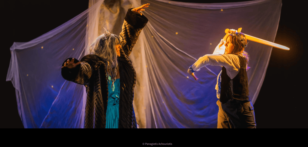 Deux acteurs en costume sur scène, l'un brandissant une épée lumineuse et l'autre gesticulant dans une robe noire, avec un arrière-plan drapé et des éclats de lumière.