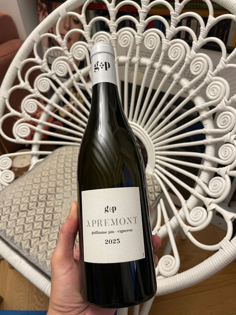 Une bouteille de vin Apremont de Guillaume Pin, portant l'étiquette g.p, présentée devant une chaise en rotin.