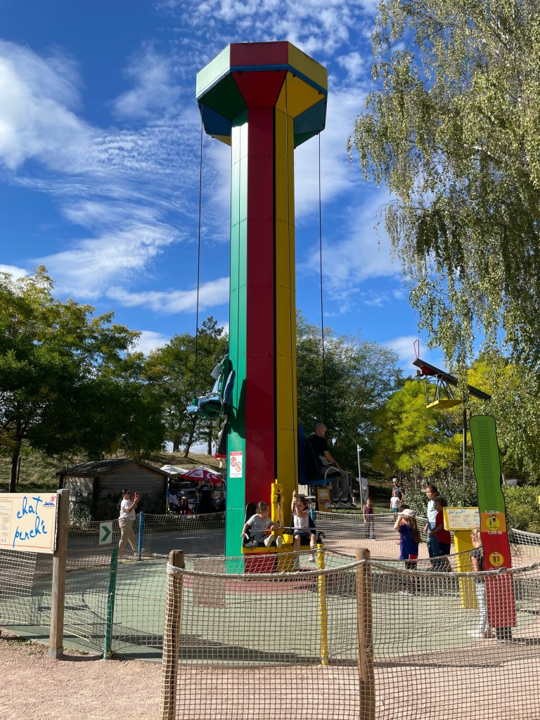Un grand totem coloré avec des balançoires, entouré d'enfants et d'adultes dans un parc.