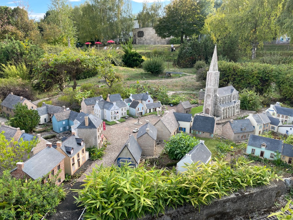 Une maquette d'un village miniature avec des maisons colorées et une église, entourée de verdure.