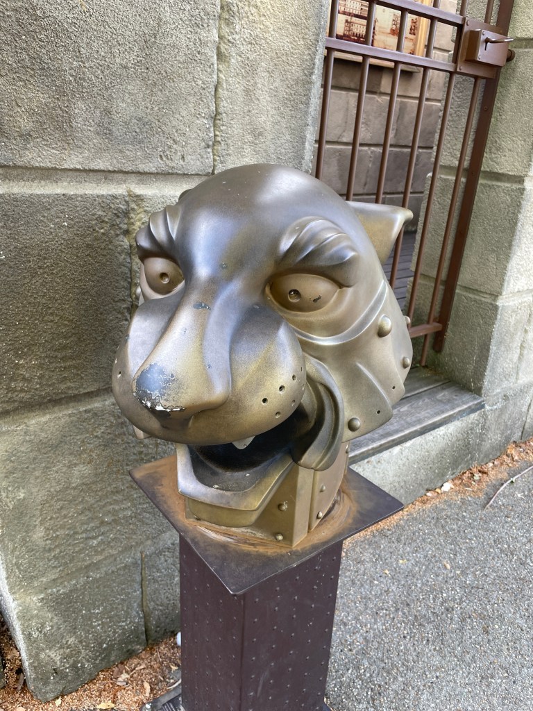 Tête de lion en métal décorative, installée sur un socle, avec des détails réalistes et des expressions animées.