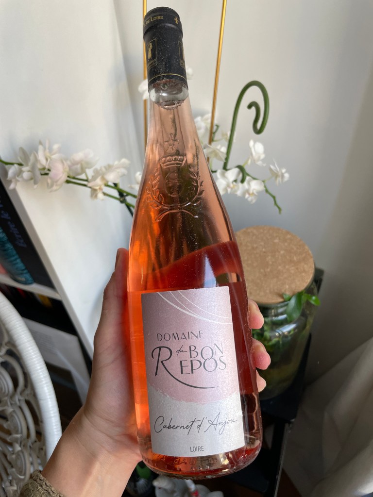 Bouteille de vin rosé 'Cabernet d'Anjou' du Domaine du Bon Repos, posée dans une main, avec des fleurs blanches en arrière-plan.