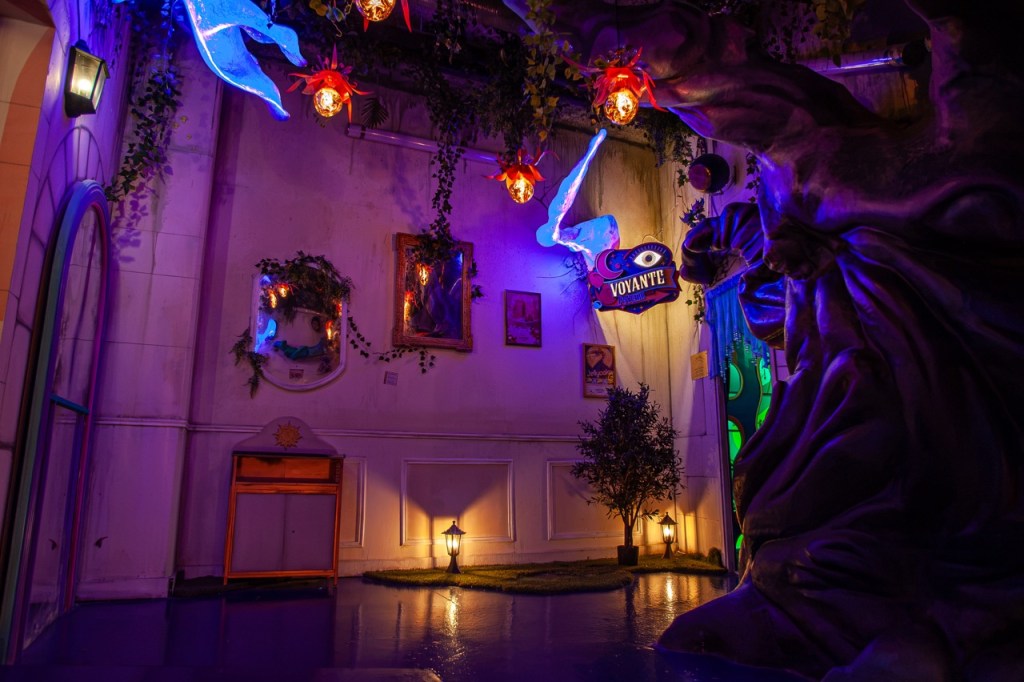 A vibrant and whimsical room featuring colorful lighting, mystical decor, and plant elements, including a twisted tree sculpture and glowing lanterns, creating an enchanting atmosphere.